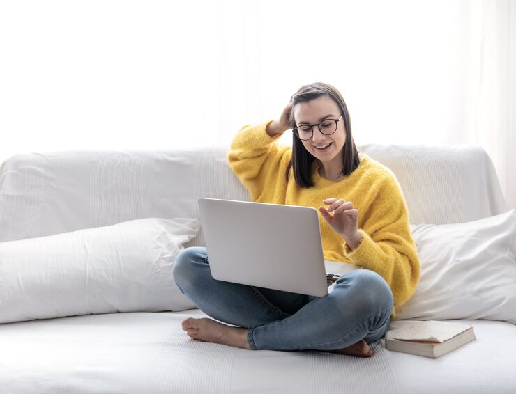 stylish-brunette-girl-yellow-sweater-sits-home-sofa-bright-room-works-laptop-remotely_169016-10242